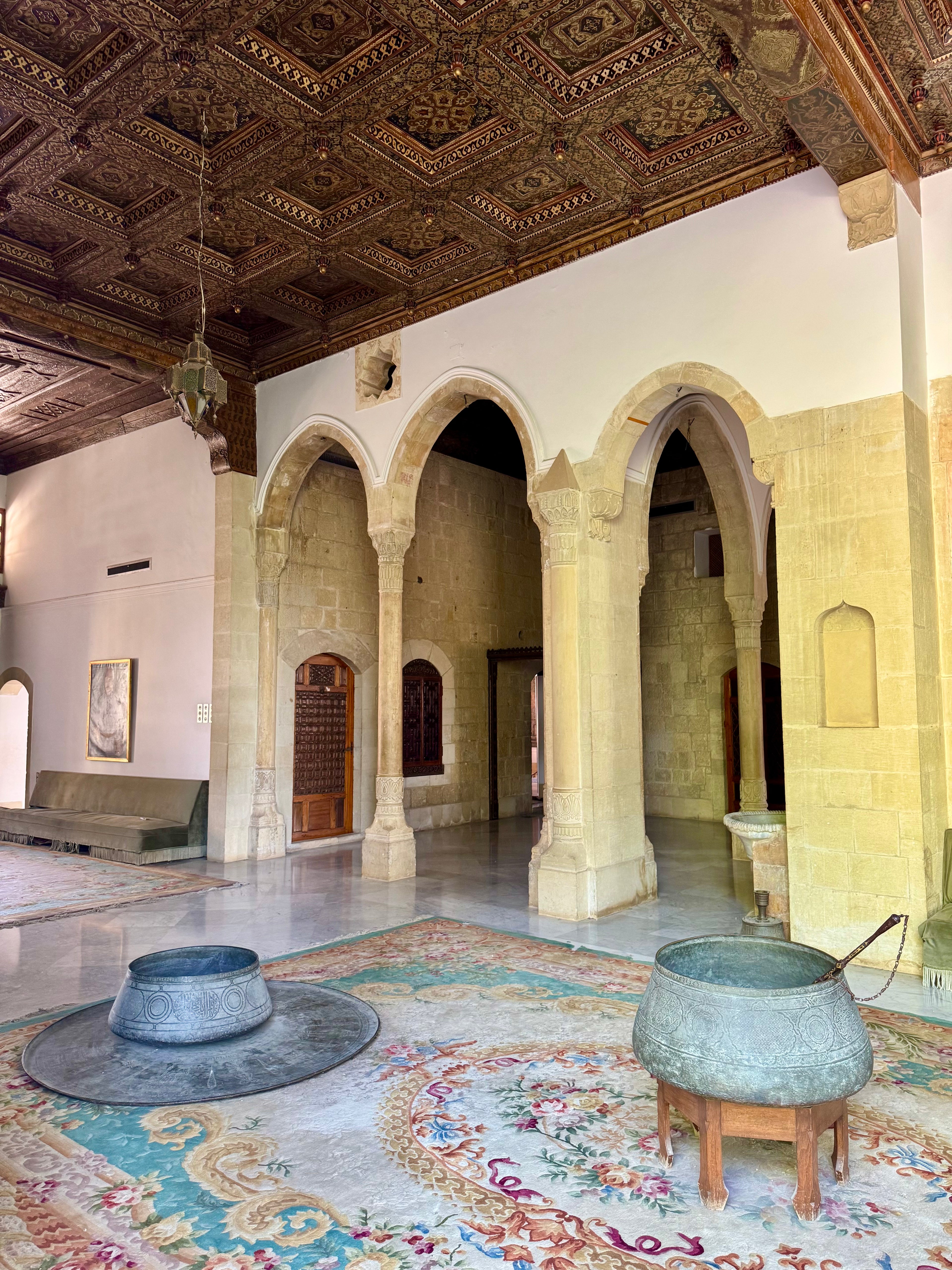 Large hall with arched doorways, decorative ceiling, and patterned rug.